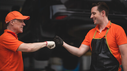 Senior and young male automotive mechanics and co-workers giving high-five as a gesture for good...