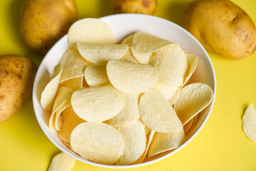 Crispy potato chips on the kitchen table and fresh raw potatoes on yellow background, Potato chips snack on bowl