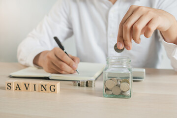 Fototapeta na wymiar Close up hand of young asian businessman puts a coin into the jar to calculate and financial plans to spend enough money on his income for saving money.