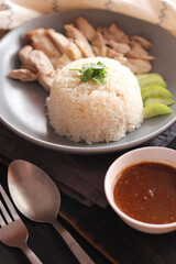Hainanese chicken rice served with dipping sauce and hot broth on a black wooden table.