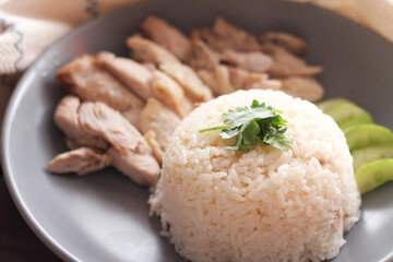 Hainanese chicken rice served with dipping sauce and hot broth on a black wooden table.