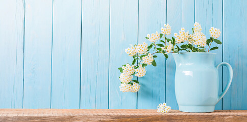 Blue ceramic jug with small white flowers on a wooden shelf. Summertime background