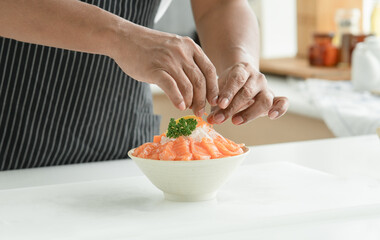 Senior man hand is decorating and prepare sliced salmon sashimi laid out on ice in a white Japanese...