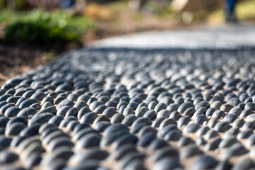 Fototapeta premium Selective focus on decorative pattern of river rocks laid in garden footpath. 