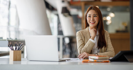 Smiling Asian businesswoman working on a laptop in a modern office, Concept of accountant, financial, expert, analyze, business report graph finance chart corporate economy, banking market research 