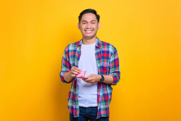 Smiling young Asian man in plaid shirt holding money banknotes and looking at camera isolated on...