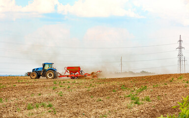 An agricultural tractor with a trailed seeder cultivates the soil in the field by applying the necessary fertilizers.