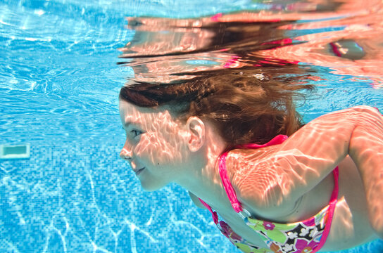 Child swims underwater in swimming pool, healthy active little girl dives and has fun under water, kid fitness and sport on family vacation 