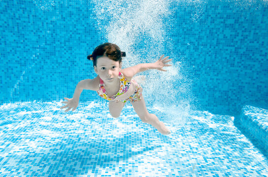Child jumps and swims in swimming pool underwater, little active girl dives and has fun under water, kids fitness and sport in pool