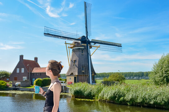 Young girl travels on vacation in Holland, looking at Dutch windmill from barge boat in canal, cruise trip in houseboat in Netherlands