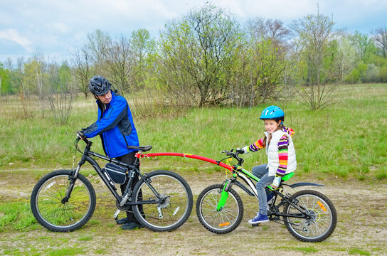 Family cycling, father teaches child to ride bicycle with bike tow bar, family sport and activity with kid outdoors