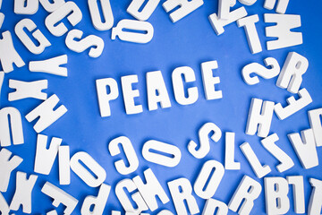 Group of loose white letters forming the word peace on a blue background together with loose letters around it. Concept text