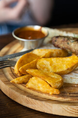 Business lunch in a cafe. Baked potato slices with tomato sauce on a wooden platter. Vertical orientation, close-up, no people