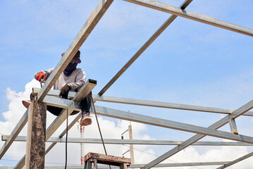 Steel worker welding structure of factory rooftop in construction site.