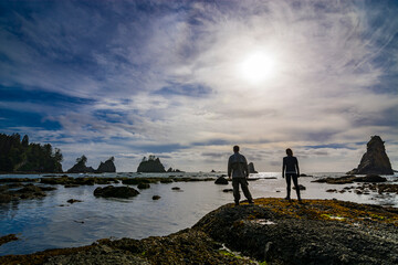 Adventurous athletic man and woman standing on a rugged Pacific Northwest beach.