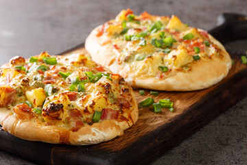 Open pie with cheese, potatoes, onions and bacon close-up on a wooden board on the table. horizontal