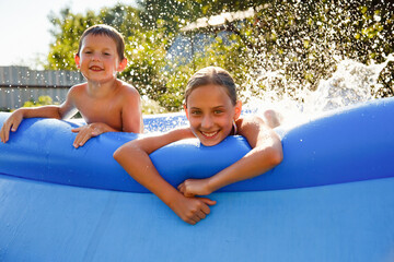 Summer season concept background. Happy friends in an inflatable pool in the garden, refreshing themselves in hot weather.