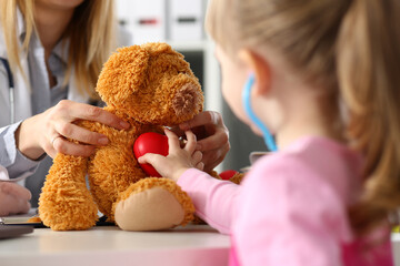 Little girl touch heart of stuffed teddy bear, listen with stethoscope, check heartbeat