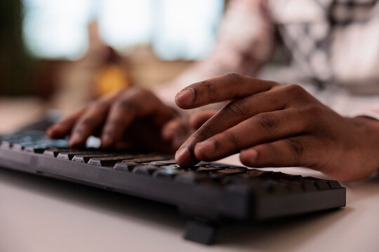 Closeup of african american male content creator writing post for social media on computer keyboard in home living room. Selective focus on man hands working remote typing blog article.
