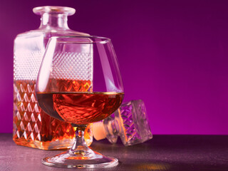 glass textured square bottle and glass goblet with amber alcohol brandy scotch whiskey bourbon. violet. Horizonal