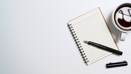 Notebook, coffee cup and pen on white background. Top view with copy space