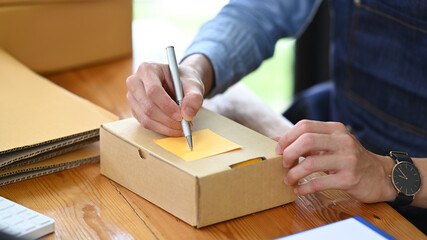 Cropped shot start up business entrepreneur writing address on cardboard box while preparing parcel boxes of product for delivery - obrazy, fototapety, plakaty