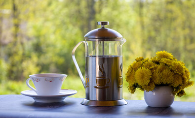 Teapot with tea and dandelion flowers. Tea in nature. Blurred background.