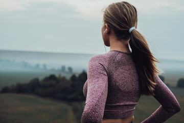 Close Up Back View of Sporty Young Woman Listening Music While Standing on the Top of Hill and Looking to the Horizon