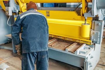 Worker cuts metal on mechanical guillotine machine in production hall. Industrial equipment for...