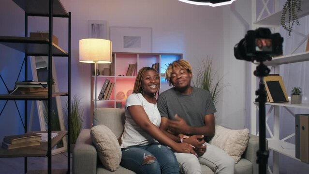 Couple vlog. Home live streaming. Family interview. Happy cheerful influencers greeting waving hello recording video content on camera on tripod in modern interior.