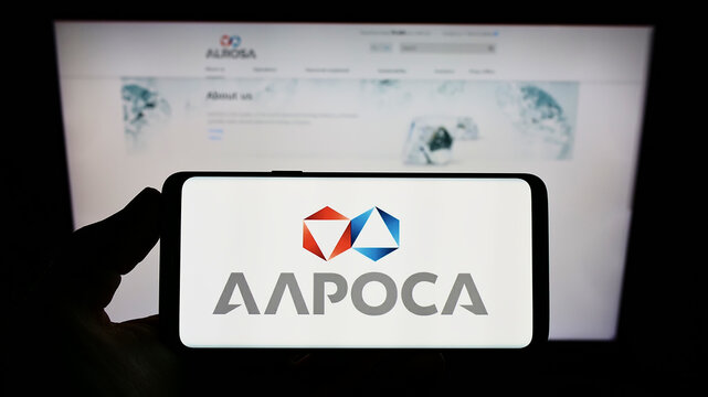 Stuttgart, Germany - 05-15-2022: Person holding smartphone with logo of Russian diamond mining company Alrosa PJSC on screen in front of website. Focus on phone display.