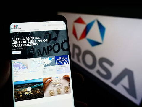 Stuttgart, Germany - 05-15-2022: Person holding smartphone with website of Russian diamond mining company Alrosa PJSC on screen in front of logo. Focus on center of phone display.