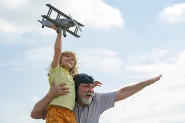 Keuken foto achterwand Oud vliegtuig Jonge kleinzoon en oude grootvader die plezier hebben met het vliegtuig buiten op de hemelachtergrond met kopieerruimte. Kind droomt van vliegen, gelukkige jeugd met opa.