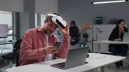 Creative engineer lift vr headset and use smartphone sitting at desk in modern office