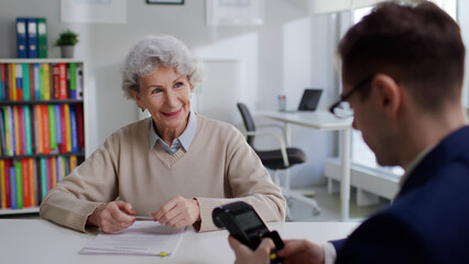 Happy elderly woman take contract and pay insurance fee with credit card