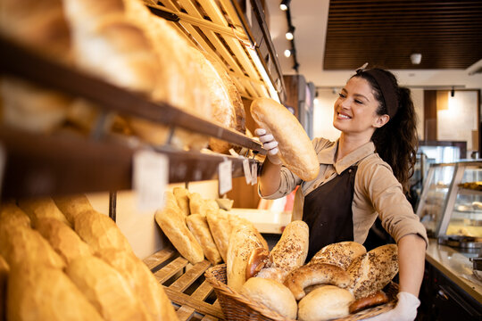 Happy smiling bakery worker placing loaf of bred on the shelf ready for sale.