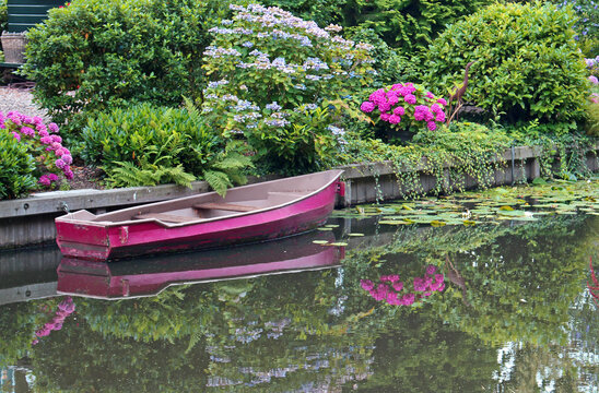Romantic image of the river Eem in Amersfoort (Netherlands), a pink rowing boat and garden with flowers. Reflections in the water