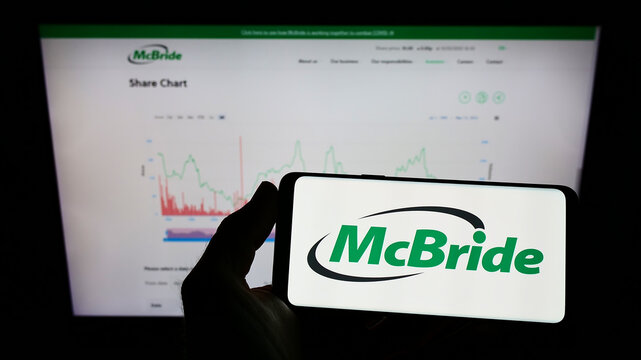 Stuttgart, Germany - 05-15-2022: Person holding smartphone with logo of British household goods company McBride plc on screen in front of business web page. Focus on phone display.