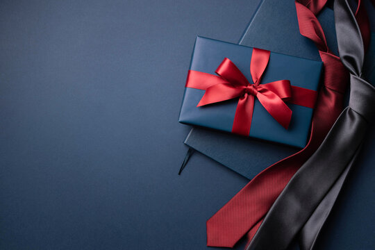 Blue gift box, notebook and neckties on dark blue background.