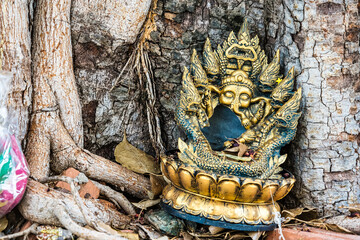 old clay broken statue of the hindu god are laid under a tree in a Thai temple.