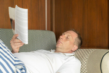 A man lies down on a sofa reading a book