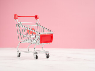 A mini shopping trolley over a marble floor with a pink background