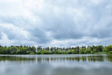 Spring landscape out of focus with noise, grain and film effect with big lake, forest trees, pines and willows with clouds before rain, tourism concept, countryside, wallpaper and cover