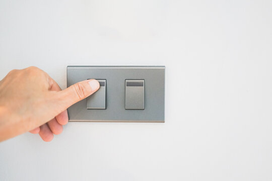 Close Up Of Adult Thumb Turn On Or Off On Grey Light Switch On White Concrete Wall At Home. Double Light Switch For Power, Energy, Environment, Saving Electrical Concept