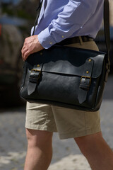 Part photo of a man with a black leather briefcase with antique and retro look. Outdoors photo