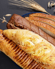 Different kind of natural breads. Fresh loafs of bread in the blue basket with ears of rye and wheat on a black background. Crunchy french baguettes. Soft focus style, closeup