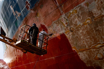 Workers working in a shipyard and painting in naval industry