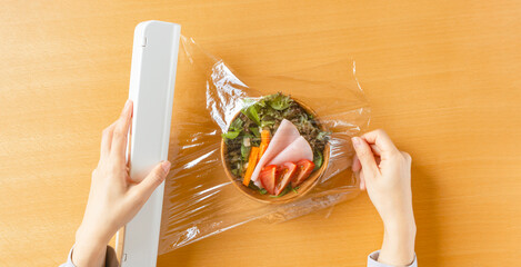 Woman preserving salad with cling wrap for foods. Preserve food, keep fresh, etc. 食品用保存のラップを用いてサラダを保存する女性。食品保存、鮮度を保つなど - obrazy, fototapety, plakaty
