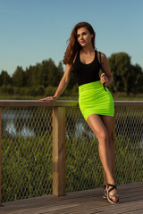 Fashion model posing outside in black color bodysuit and green mini skirt.