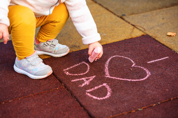 A small child draws a chalk inscription on the ground. I love Dad. Top view. Father's Day concept